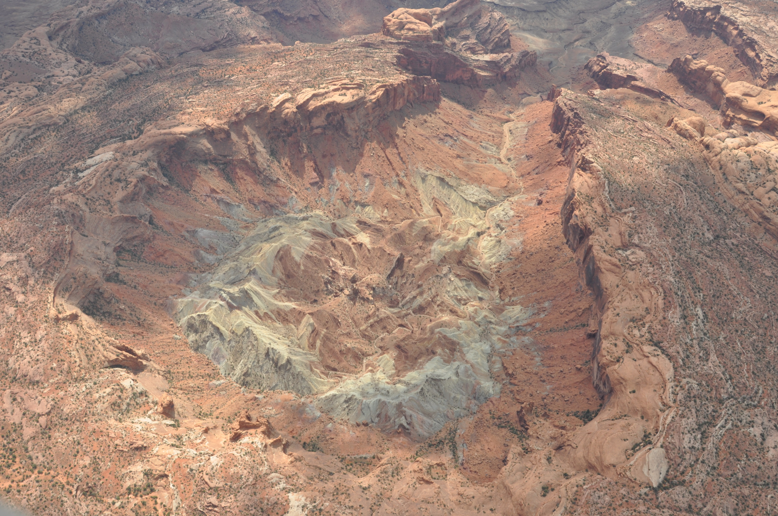 Aerial view of the Upheaval Dome, a geological formation in Canyonlands National Park, Utah. This intriguing structure, possibly shaped by a meteor impact, displays concentric rings of rock layers in red, brown, and gray hues nestled amid the desert terrain.