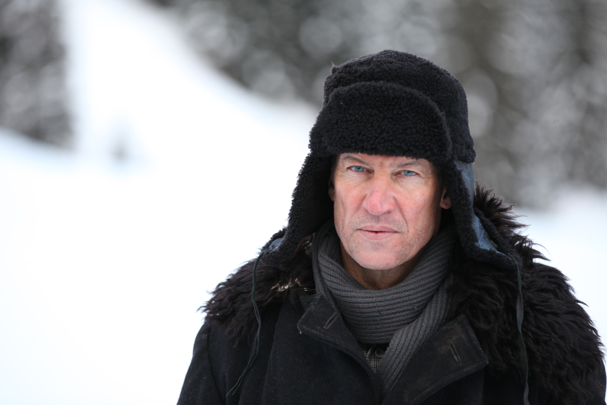 A person in a black coat and fur hat stands in a snowy landscape, reminiscent of 