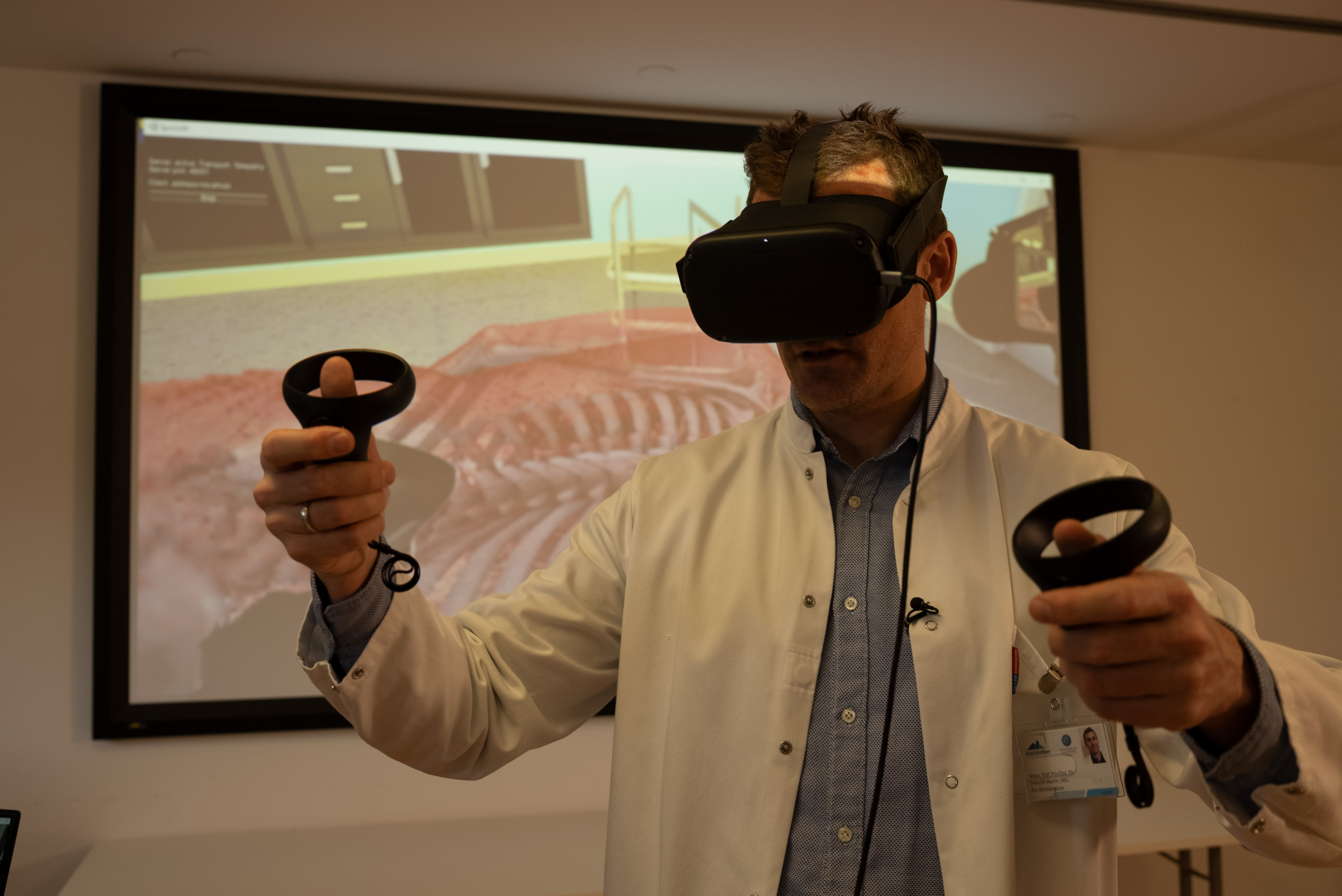 A person in a white coat uses a virtual reality headset and controllers, embodying the future of virtual medicine. A large screen in the background displays an anatomical image, underscoring the integration of innovative technologies into modern healthcare practices.