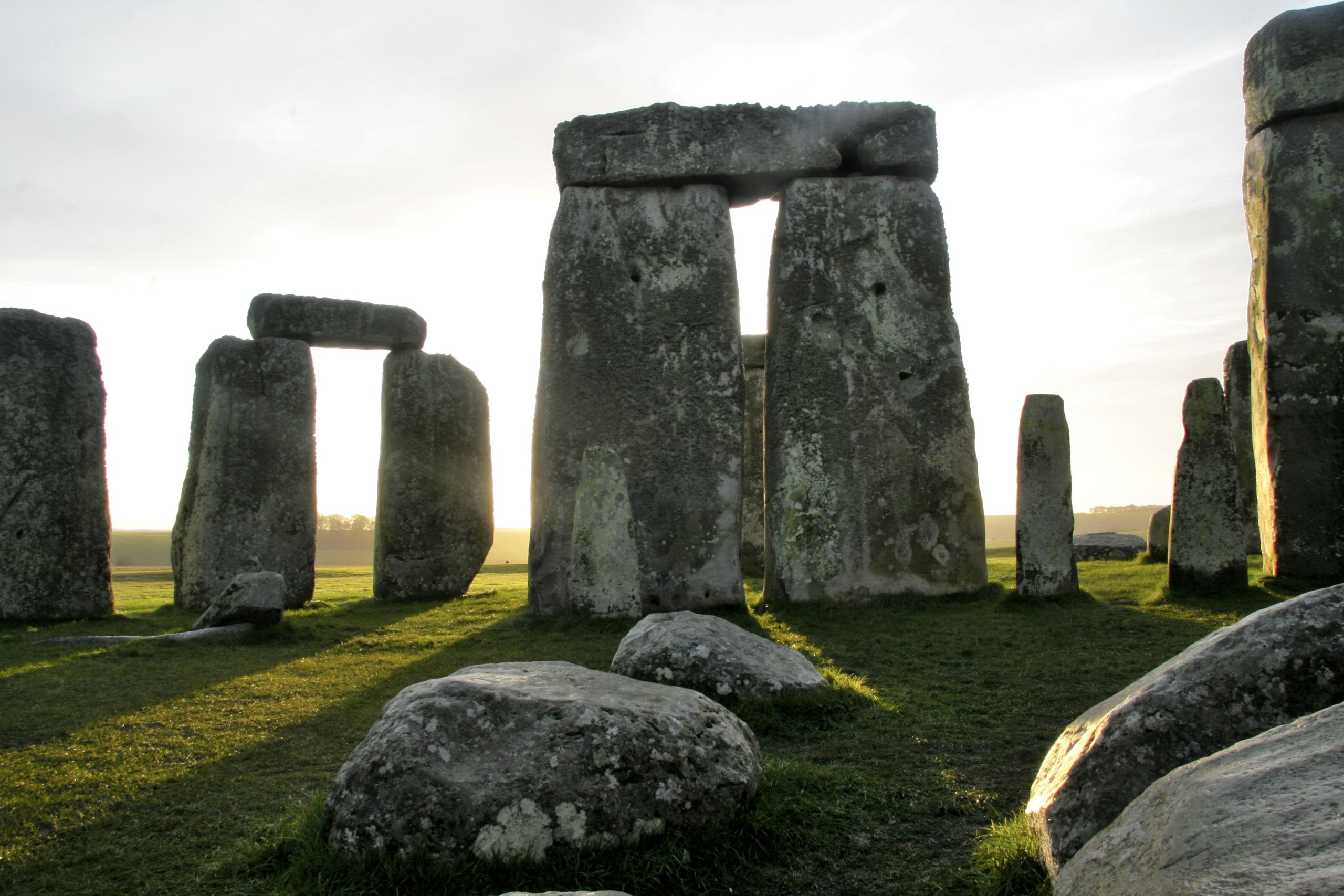 At dawn, Stonehenge emerges with its majestic stone monoliths arranged in a circular formation. The sunlight casts long shadows on the grassy ground, enhancing the serene and ancient atmosphere of this iconic site.