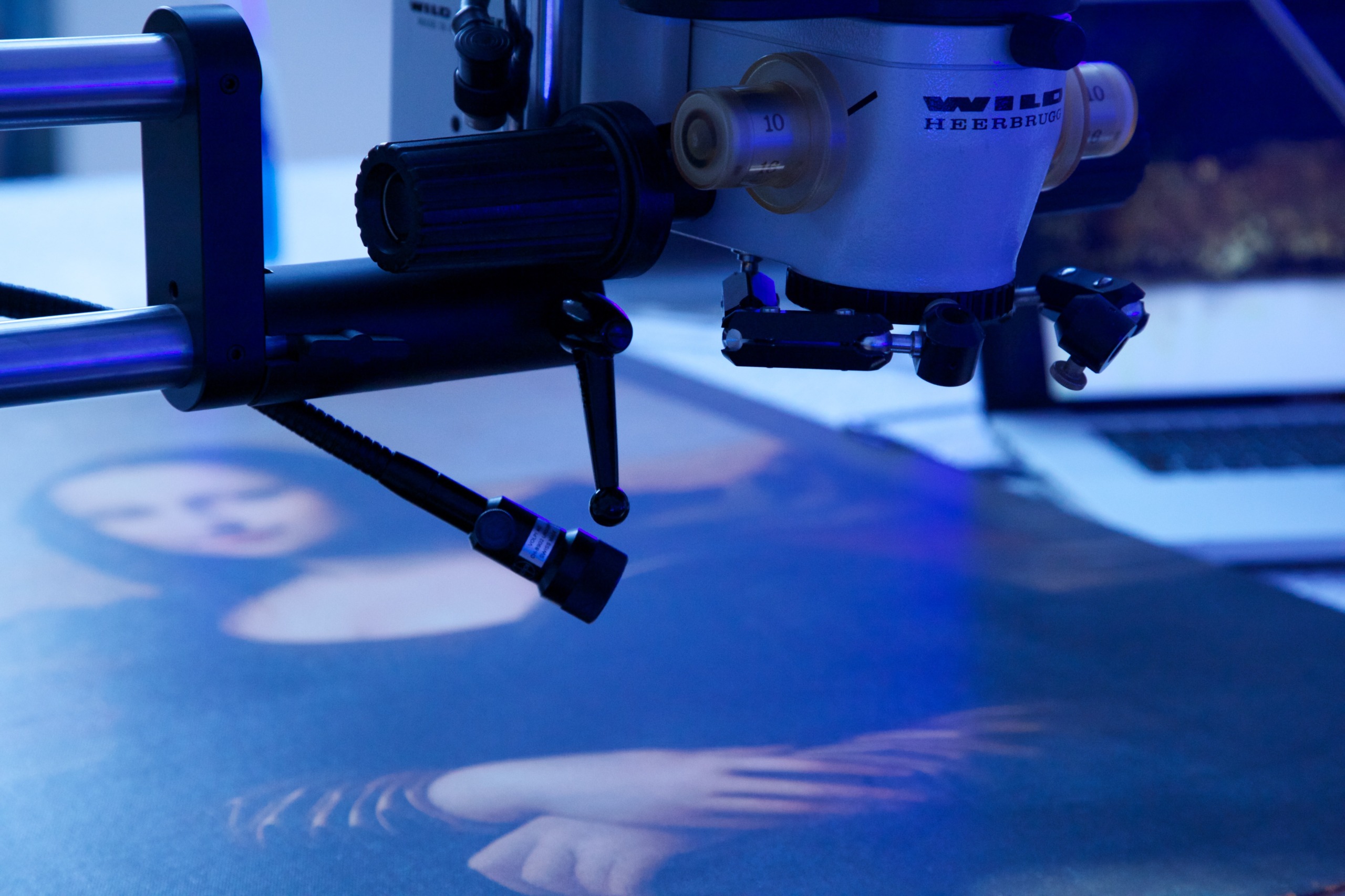 A close-up of a high-tech microscope reveals the enigmatic smile of a Mona Lisa-like artwork under examination. Bathed in blue light, the precision equipment meticulously analyzes the painting's surface.