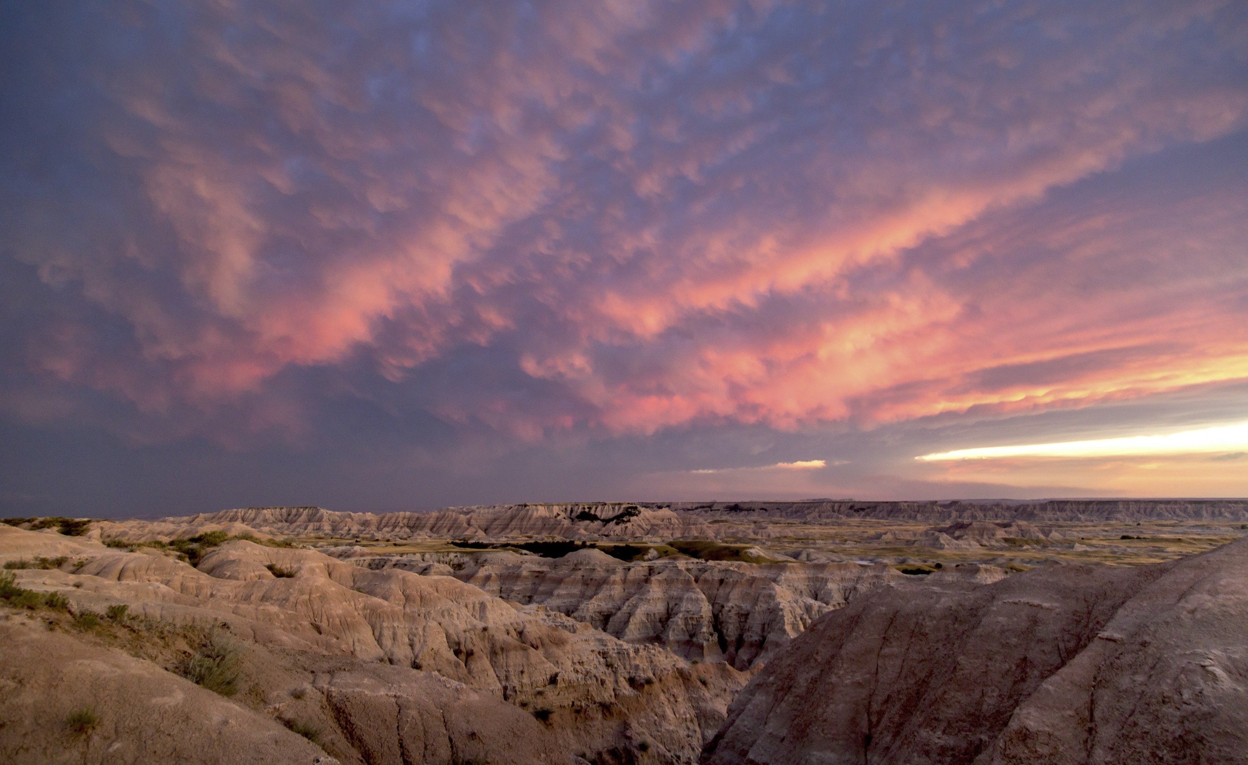 A stunning landscape of rugged, eroded rock formations under a dramatic sky captures a magic moment. The sky is filled with pink and purple clouds, suggesting a sunrise or sunset, casting a warm glow over the rocky terrain below in this spell of nature.