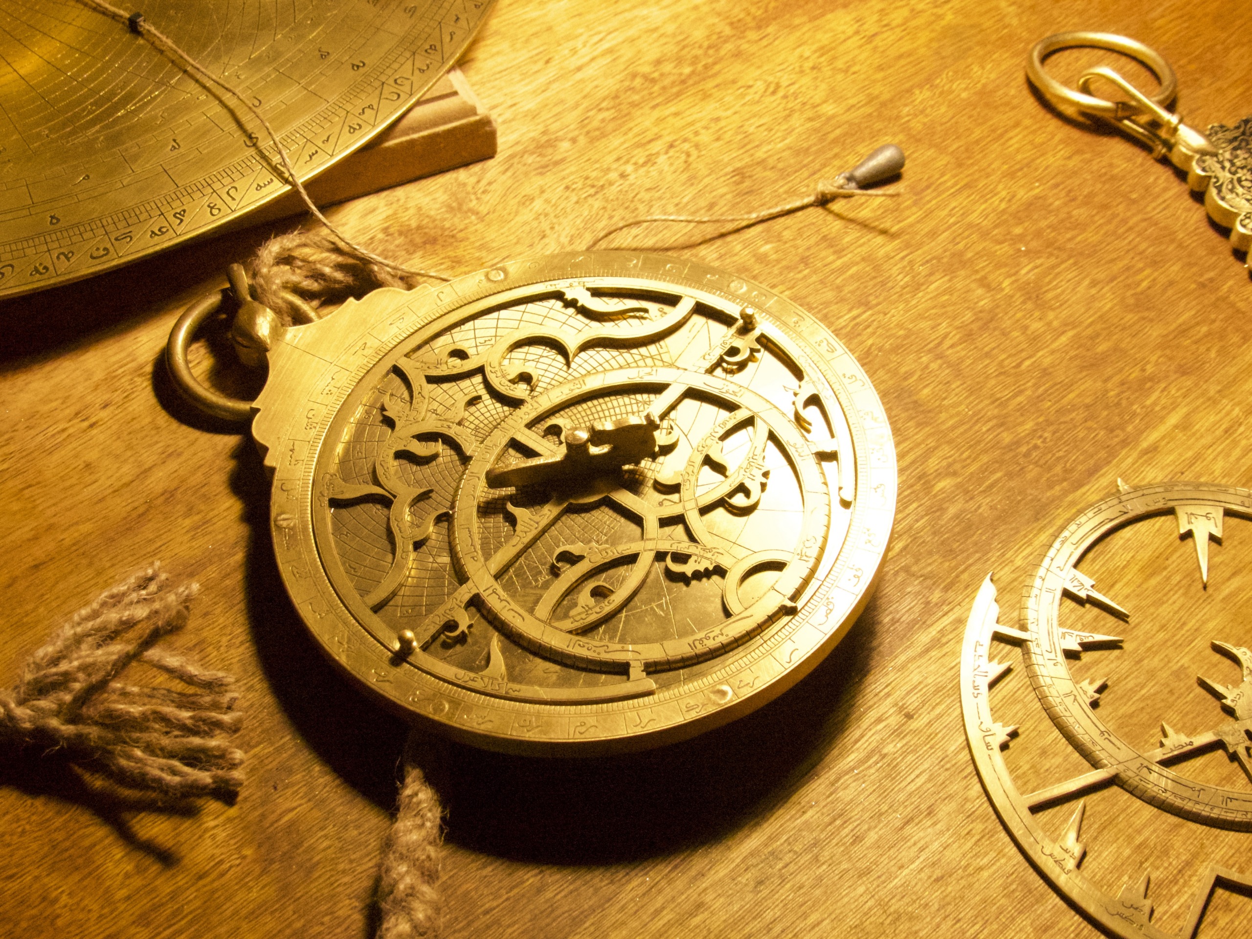 A collection of vintage brass astrolabes, reminiscent of Star Chasers from Senegal, rests on a wooden table. The intricate designs and gears are illuminated by warm light, showcasing their detailed craftsmanship. A rope is attached to the largest astrolabe.