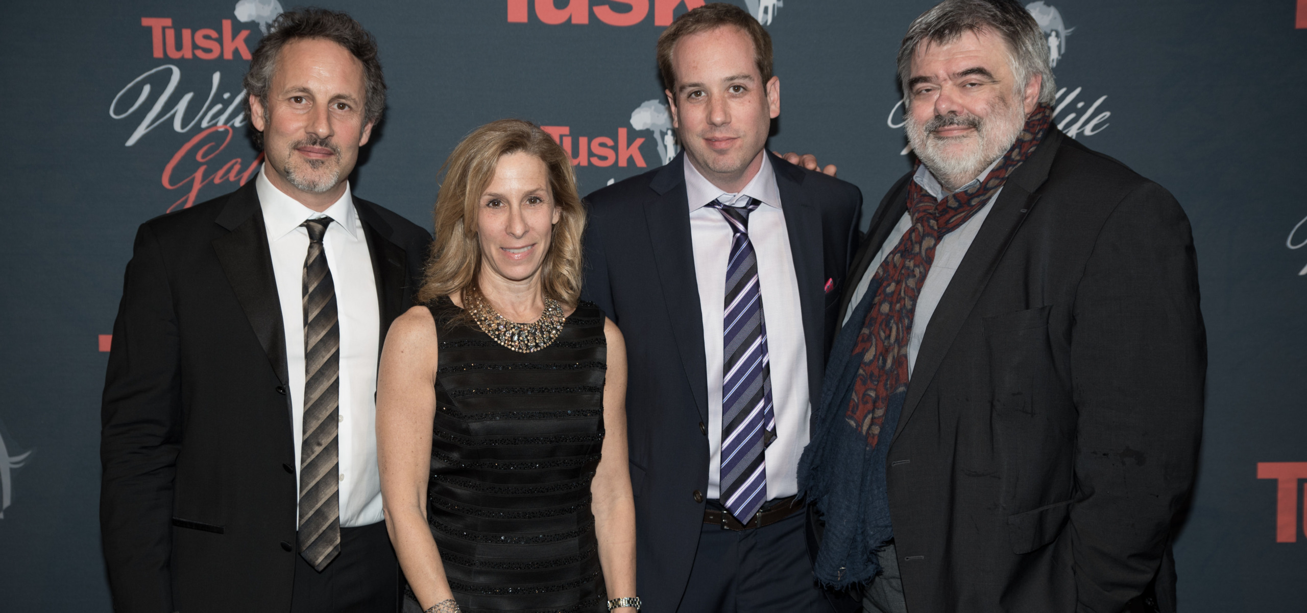 Four people pose together in formal attire against a backdrop featuring the word Tusk and an outline of Africa. Three men in suits and a woman in a black dress smile at the camera, celebrating their honor with the Game-Changer Award.