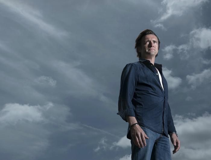 A person stands confidently under a cloudy sky, wearing a dark shirt and jeans, reminiscent of a scene worthy of Terra Mater productions. They look off into the distance, where the dramatic sky adds depth and atmosphere to the image.