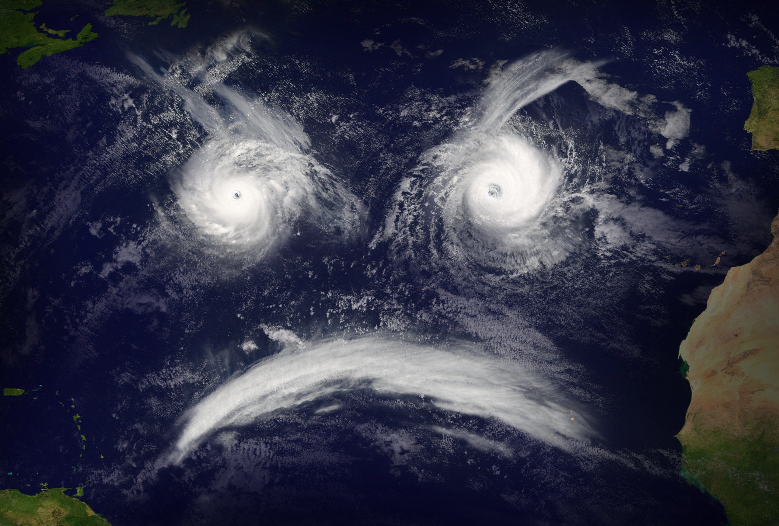 A satellite image captures the metamorphoses of two hurricanes in the Atlantic, their swirling patterns resembling eyes, while a curved line of clouds below forms a frowning mouth. Landmasses are visible on the left and right edges, framing this dramatic scene.