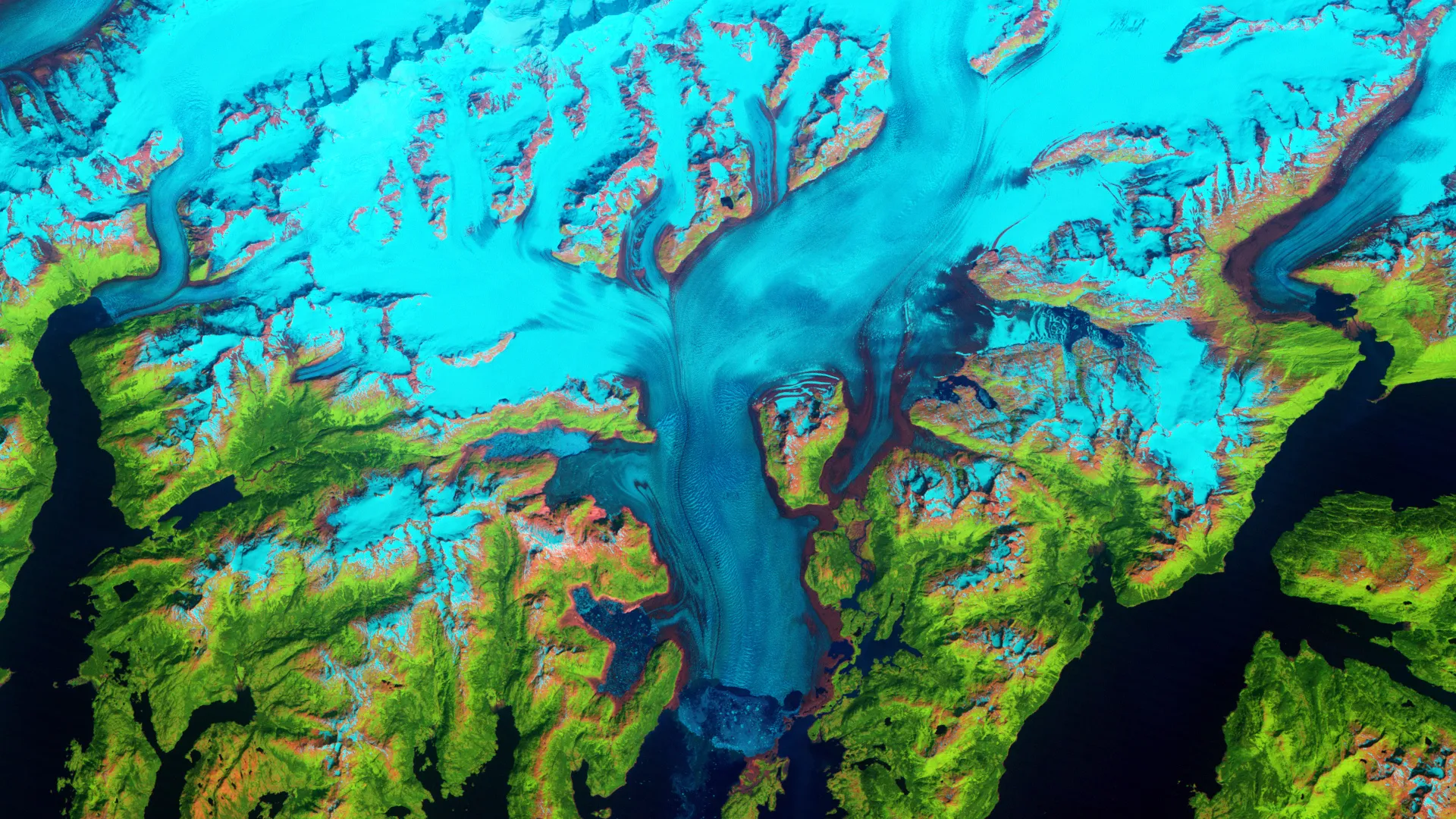 Satellite image of a vibrant landscape with glacial blue ice, intricate patterns of white snow, and lush green land. Deep blue water bodies surround the area, creating a striking contrast.