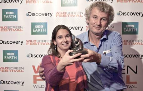 Two people proudly stand together, holding an award that celebrates their success. They are smiling in front of a backdrop featuring logos for Wildscreen 2012, BBC Earth, and Discovery.